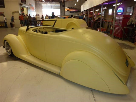Yellow vintage car on display in a showroom with people around