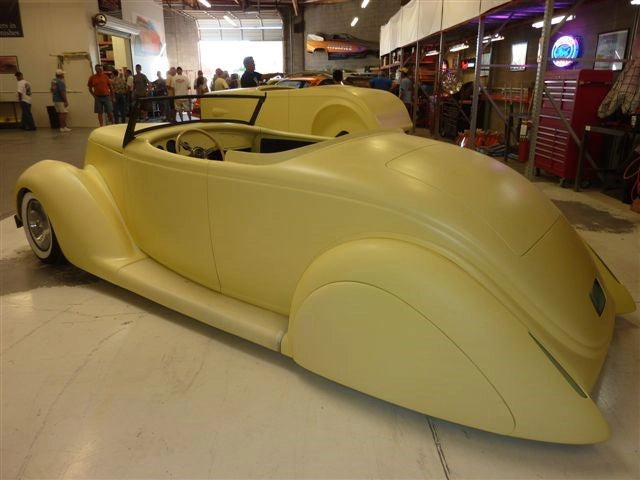 Yellow vintage car on display in a showroom with people around